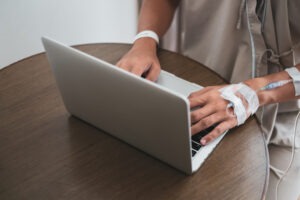 An injured man in a hospital gown is using a laptop to research Fort Worth personal injury lawyers.