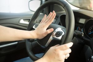 Driver pressing car horn with both hands on steering wheel, emphasizing aggressive driving and road rage risks
