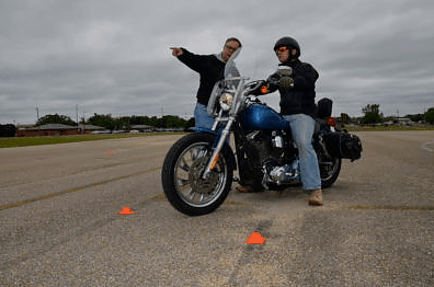 Motorcycle safety training with instructor guiding rider through cone course on overcast day