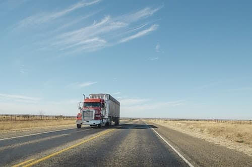 Red semi-truck driving on a two-lane rural Texas highway under clear blue sky, emphasizing risks of truck accidents on open roads