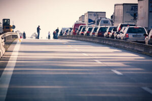 Traffic jam on highway with cars and trucks stopped in lanes, people standing outside vehicles after major road incident.